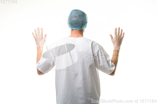 Image of A male doctor stands with his hands raised up, gloves are on, a mask and a hat are on his head, rear view