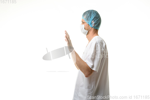 Image of A male doctor stands with his hands raised up, gloves are on, a mask and a hat are on his head, side view