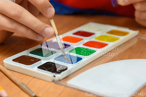 Image of The child\'s hands are dipping with a brush in the desired color of watercolor paints