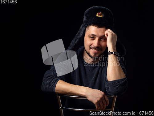 Image of Portrait of a smiling man of thirty years of Caucasian appearance in a Soviet officer\'s fur hat on a black background