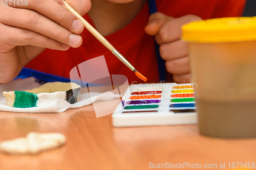 Image of A girl dips a brush in paint of the desired color while painting a craft from salt dough, close-up