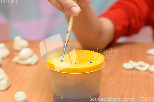 Image of A girl dips a brush into a glass of water painting figures from salt dough