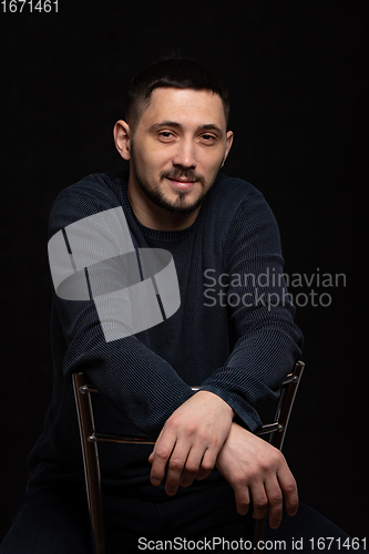 Image of Portrait of a smiling man of thirty years of Caucasian appearance in a regular sweater on a black background