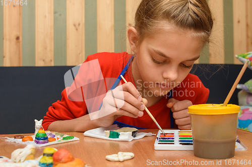 Image of A girl dips a brush in paint of the desired color while painting a craft from salt dough
