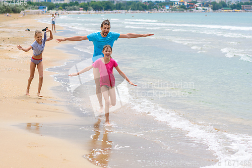 Image of Dad with two children running merrily along the seashore