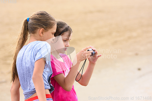 Image of Two girls look at photos on the screen of a digital camera while on the sea sandy beach