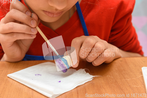 Image of A girl paints a figurine made of salt dough with a brush, close-up