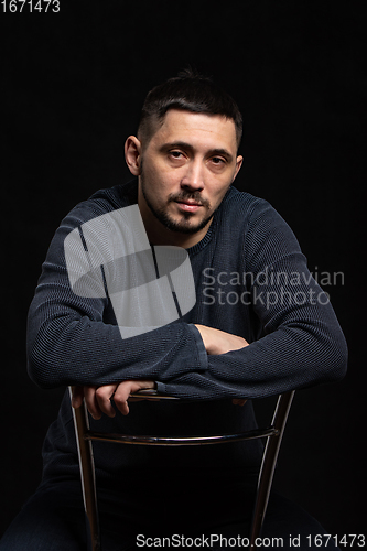 Image of Portrait of a man of thirty years of Caucasian appearance in a regular sweater on a black background