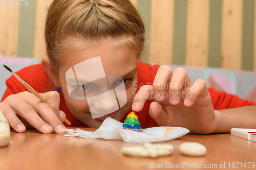 Image of A girl bending over looks at a painted figurine made of salt dough