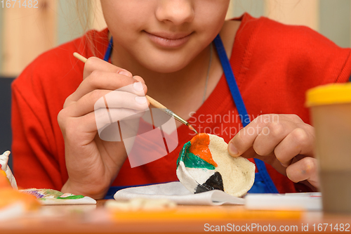 Image of A girl paints a craft from salt dough with watercolors, close-up