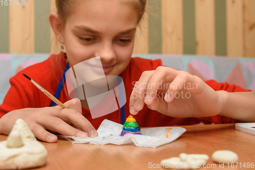 Image of Girl rejoices painting a figurine made of salt dough