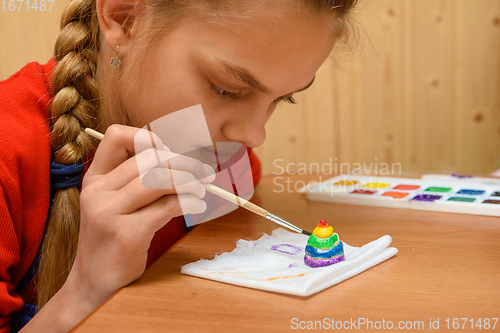 Image of A girl carefully paints a figurine made of salt dough