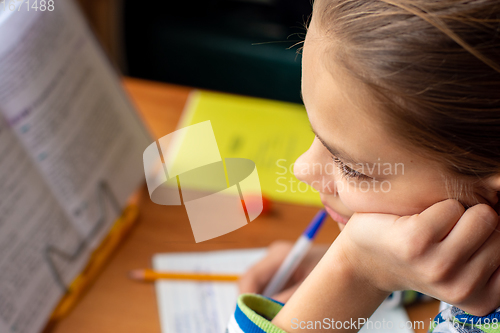 Image of Close-up of a girl doing homework, a girl lost in thought distracted from the task