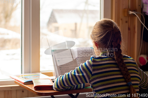 Image of Back view of a schoolgirl sitting by the window and doing homework