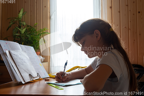 Image of Girl does homework while sitting at the table in the room of a country house