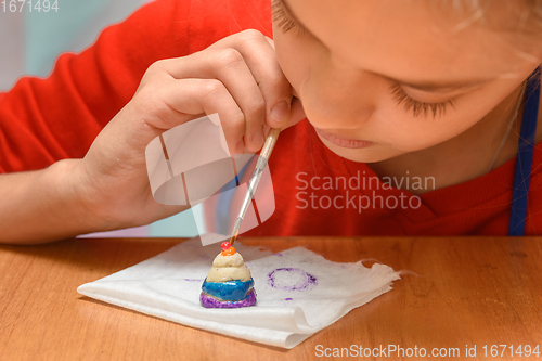 Image of A girl carefully paints a figurine made of salt dough, close-up