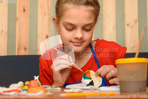 Image of A girl paints a craft from salt dough with watercolors