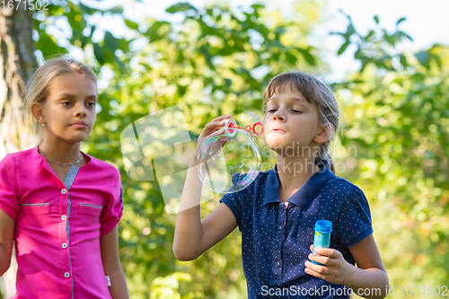 Image of A girl blows bubbles, another girl watches her closely