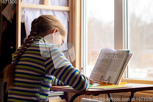 Image of Girl doing homework sitting at the table by the window