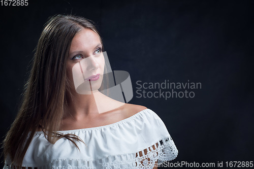 Image of Portrait of a beautiful girl looking up in a loose white dress on a black background