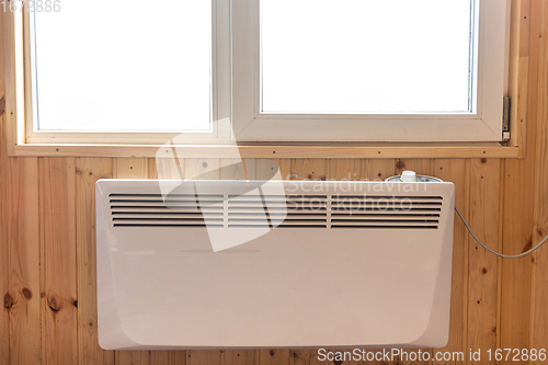 Image of Electric radiator under the window of a country house whose walls are finished with clapboard