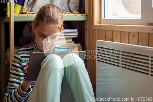 Image of The girl plays in the tablet, sitting in a secluded corner next to the battery