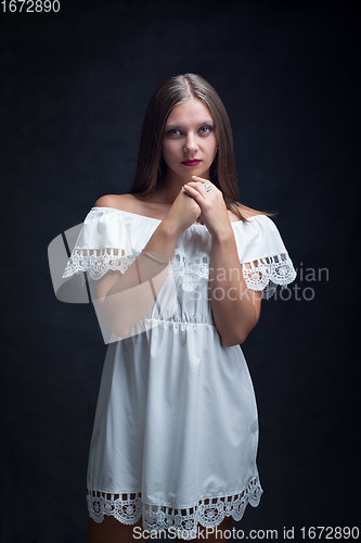 Image of Portrait of a beautiful girl in a loose white dress on a black background