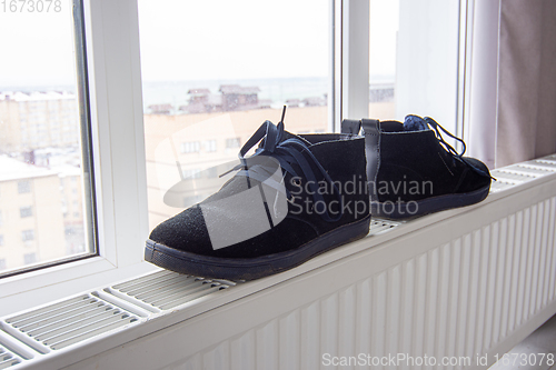 Image of Suede winter boots are dried on a radiator near the window