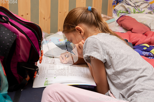 Image of Schoolgirl does her homework on a spread out couch piled high with things