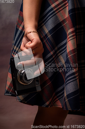 Image of Girl\'s hand holding a camera near the hem of the dress, vertical frame, studio photography on a gray background