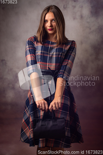 Image of Portrait of a beautiful girl on a gray background, the girl holds a black handbag with two hands in front of her