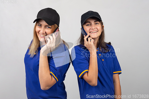 Image of Mother and daughter are standing with their backs to each other, talking on the phone and looking into the frame