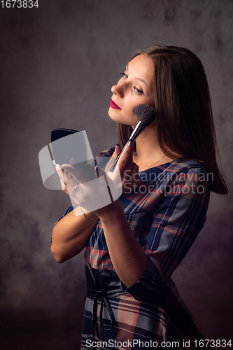 Image of Girl powders her face with a brush looking in the mirror, studio photo on a gray background