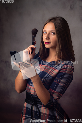 Image of The girl powders her face with a brush while looking in the mirror, the girl was distracted and looked into the frame, studio photography on a gray background