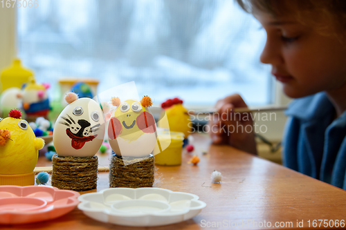 Image of In the foreground there are decorated children\'s Easter eggs, in the background a child is painting an egg