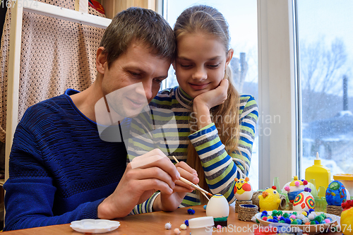 Image of Father shows the girl how interesting it is to paint Easter eggs