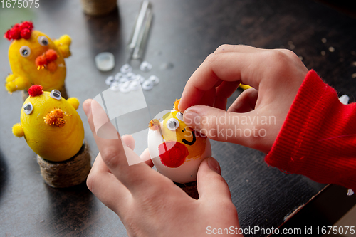 Image of A girl decorates an egg for the Easter holiday by carefully gluing funny eyes to it