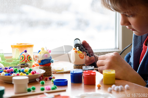 Image of A girl glues elements to an Easter egg with a glue gun