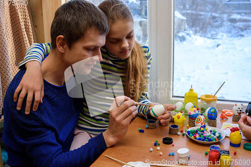 Image of Father and daughter paint easter eggs while sitting at the table by the window