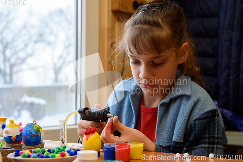 Image of A girl glues a decorative element to crafts with a glue gun