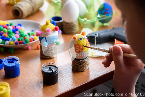Image of A girl draws a funny funny face on an Easter egg