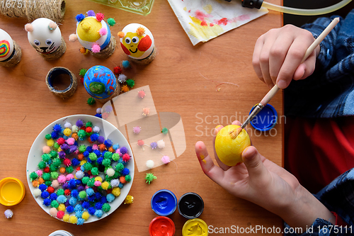 Image of Top view of the desk and the hands of a child who paints festive easter eggs with brushes