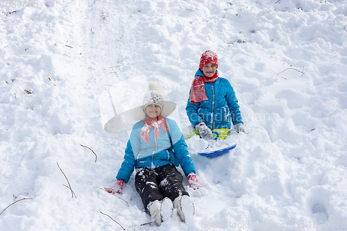 Image of Two girls rolled down the hill and sitting in the snow joyfully look into the frame