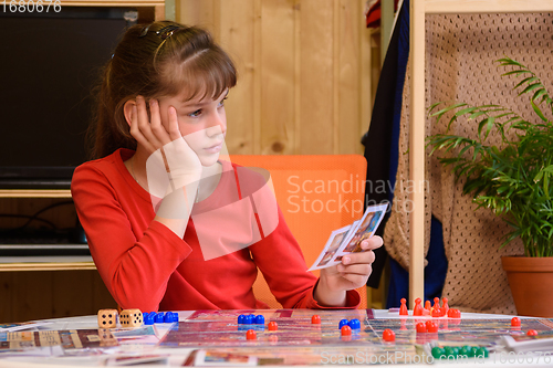 Image of The girl plays board games and is thoughtful holding cards in her hand