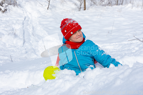 Image of A girl sits in a snowdrift and looks funny at the top of the slide