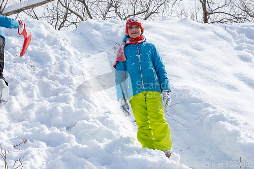 Image of Happy girl stands on the slope of a hill in winter and joyfully looks into the frame