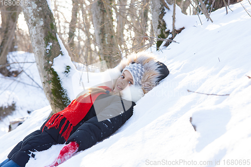 Image of The girl fell into a snowdrift with her back and looked into the frame in a snowy forest