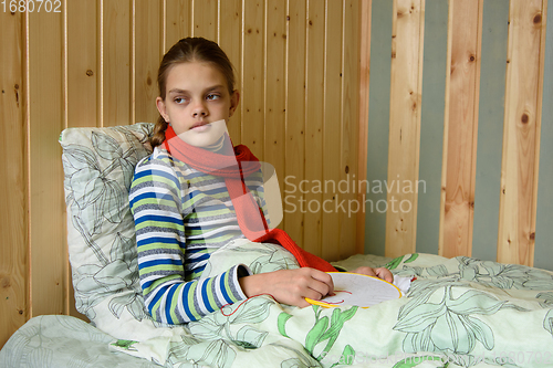 Image of A sick girl sits in bed and looks tiredly out the window