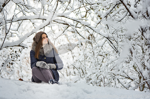 Image of The girl sat down in a beautiful snowy forest and admires the beauty