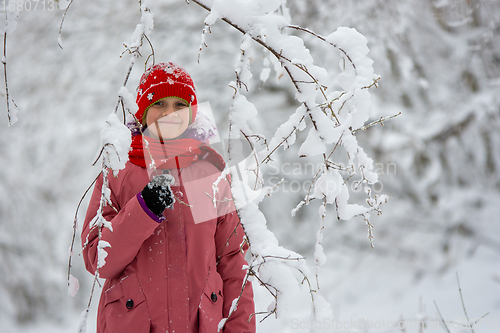 Image of Happy girl stands in a snowy forest under a snowy branch